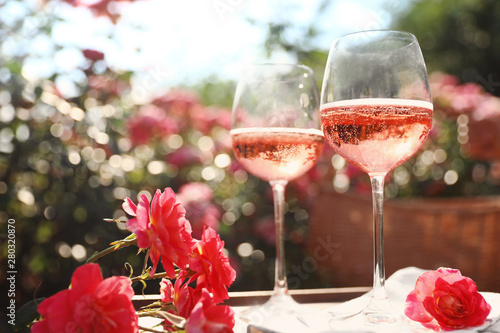 Glasses of rose wine on table in blooming garden photo