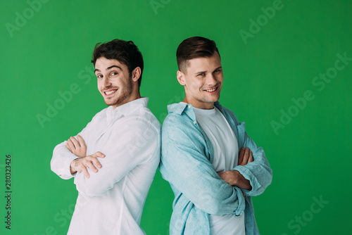 two smiling men standing with crossed arms and looking at camera isolated on green