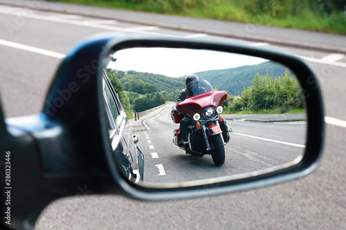 Obraz na plátně Biker riding motocycle seen by car driver in the mirror on english road