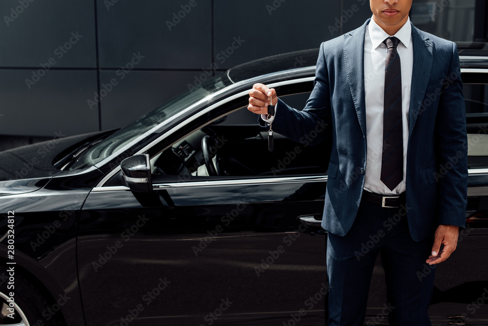 cropped view of african american man in suit holding car key cropped view of african american man in suit holding car key