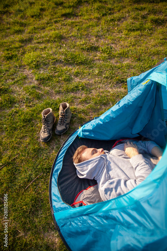 One young man, sleeping in tent, in a daylight. Sunset or sunrise sunlight.