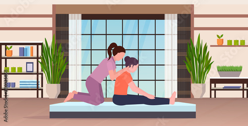 female personal trainer doing stretching exercises with girl fitness instructor helping woman to stretch muscles workout concept modern yoga studio gym interior flat full length horizontal