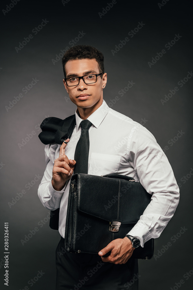 african american businessman in glasses holding blazer and leather briefcase on dark background african american businessman in glasses holding blazer and leather briefcase on dark background
