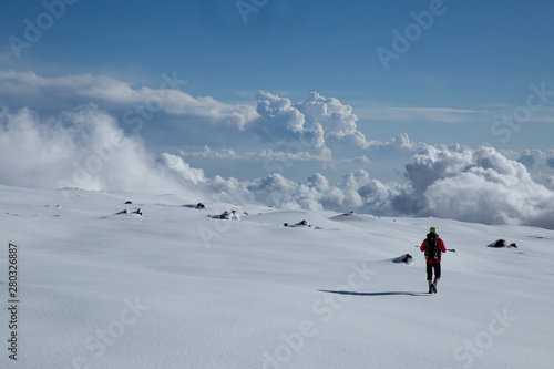 Man in shorts with small backpack walking on a snow leaving no trace. Cloudy blue color day on the glacier on the Etna volcano. Sicily, Italy