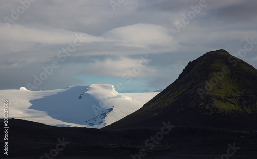 Black volcanic hill in front of white glassier with shadows and cloudy sky background. Landmannalaugar, Iceland photo