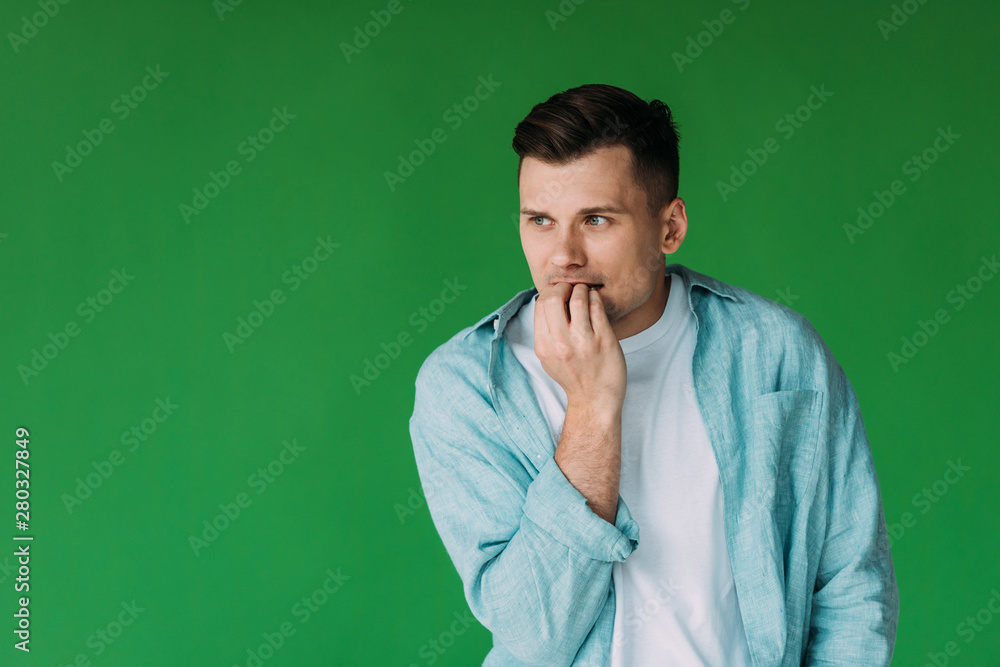 worried young man in shirt biting fingers and looking away isolated on green worried young man in shirt biting fingers and looking away isolated on green