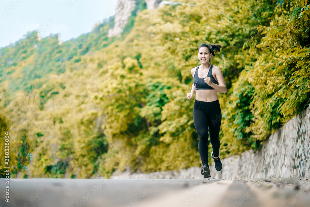 An beautiful Asian woman running and listening music over road during moring. Workout and sport outdoor concept.