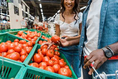 cropped view of cheerful woman neat african american man holding tomato