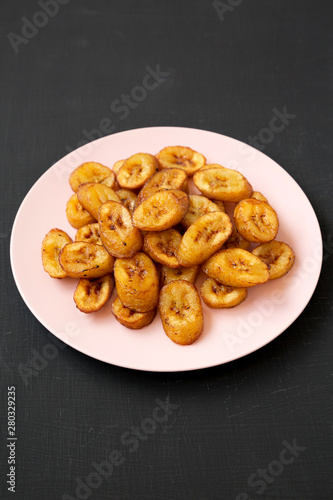 Homemade fried plantains on a pink plate on a black surface, low angle view. Close-up.