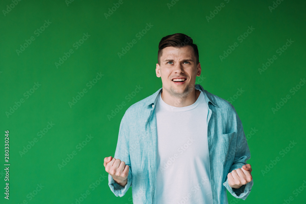 front view of irritated young man in shirt holding fists up isolated on green front view of irritated young man in shirt holding fists up isolated on green