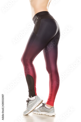 Side view of female legs in sport tights and sneakers on white background