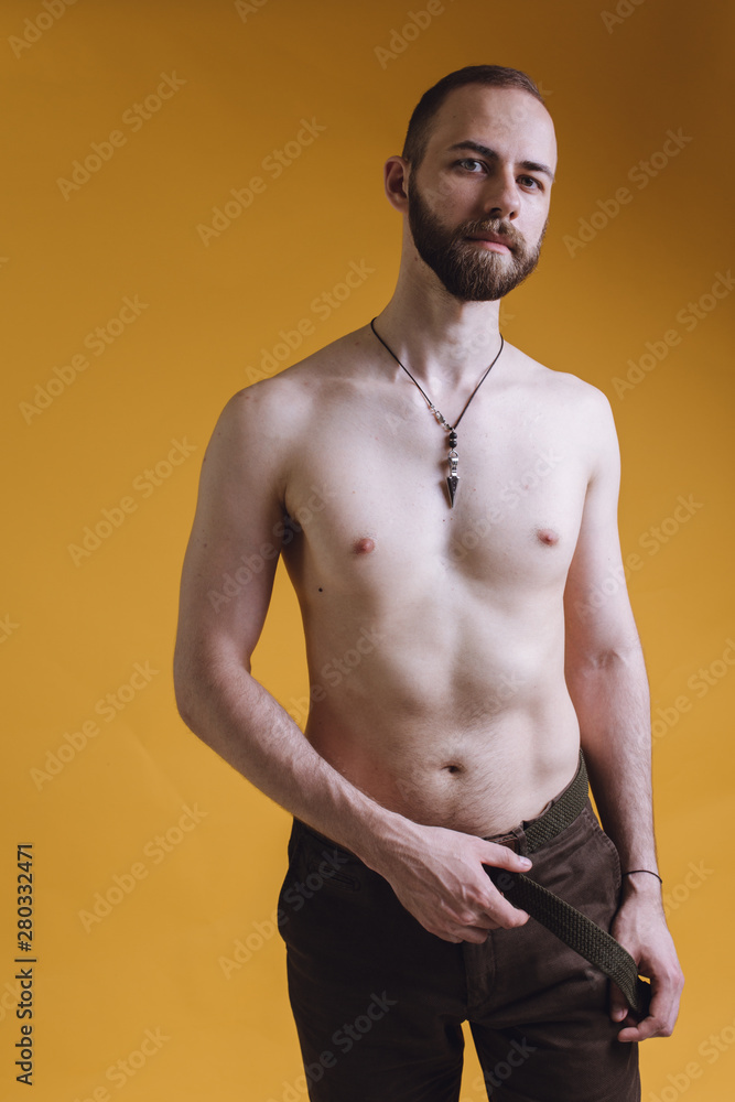 bearded man with a bare torso posing on a colored background. skinny guy  after exercise and diet. emotional portrait of a student. man with a  pendant around his neck Photos | Adobe