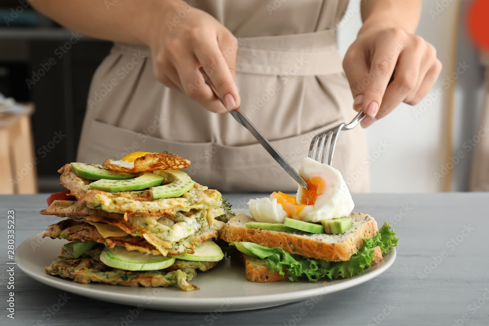 Woman eating tasty squash waffles, sandwich and fried egg at table