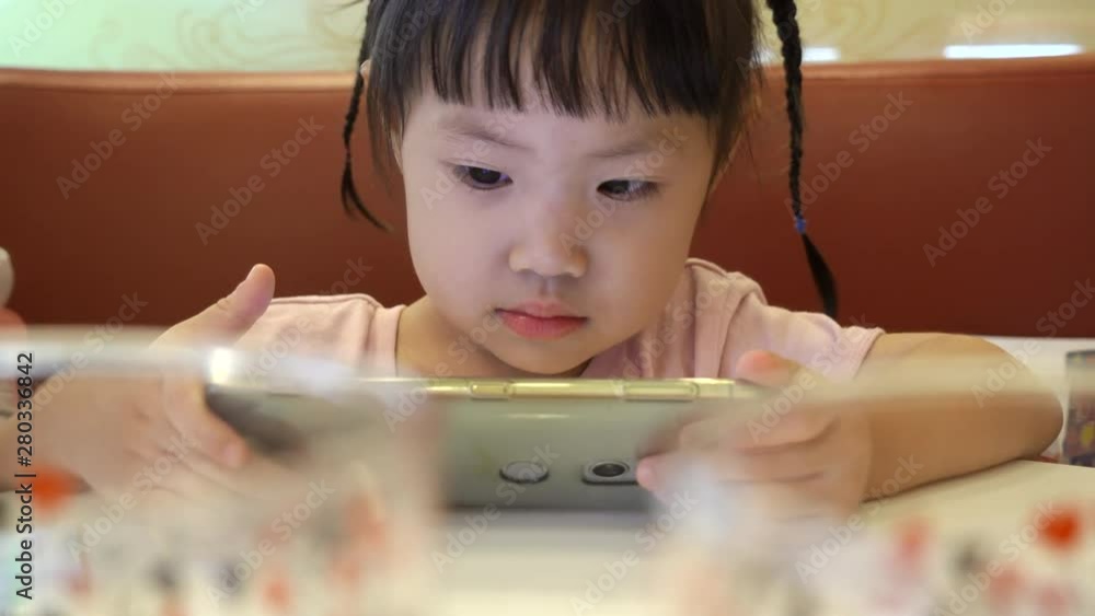 Asian baby girl watch cartoons in smartphone at restaurant in shopping mall. Handheld shot 4K Asian baby girl watch cartoons in smartphone at restaurant in shopping mall. Handheld shot 4K