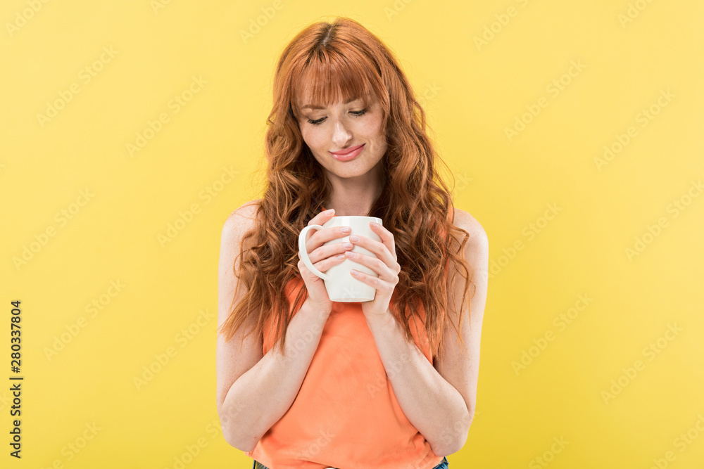 smiling redhead girl holding cup of coffee isolated on yellow smiling redhead girl holding cup of coffee isolated on yellow