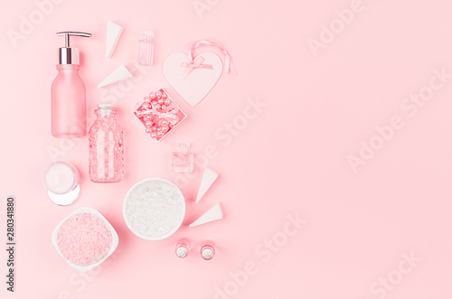 Cosmetic products and accessories in pink color - cream, bath salt, essential oil, soap, towel, pearls, bottles, heart, bowl on pink background, top view.