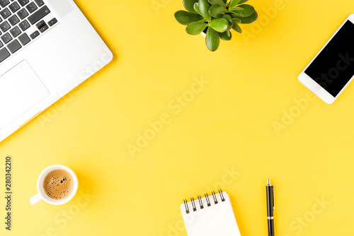 Office desktop with laptop and accessories on yellow background. Top view