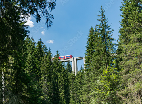 narrow gauge train crosses a long viaduct across a deep canyon in the Swiss Alps © makasana photo