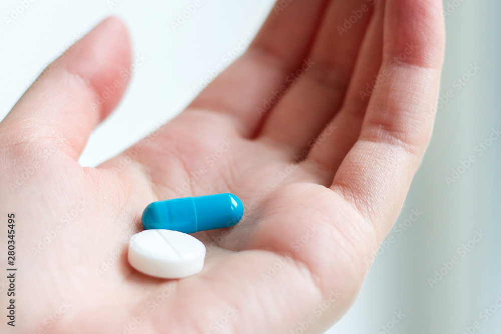 Blue and white pill capsule on the female palm on white background. Antidepressant pills in female hand. Female hand holding a pill on the palm Blue and white pill capsule on the female palm on white background. Antidepressant pills in female hand. Female hand holding a pill on the palm