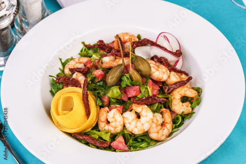 Mediterranean salad. Arugula, tomatoes, shrimps, olives, olives, basil and rosemary, dressed with olive oil and balsamic sauce, decorated with lemon and chili pepper