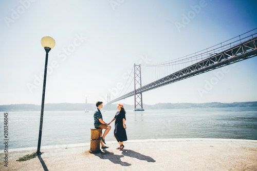 Romantic couple holding hands in front of the bridge called April 25 in Lisbon in Portugal at sunny summer day.