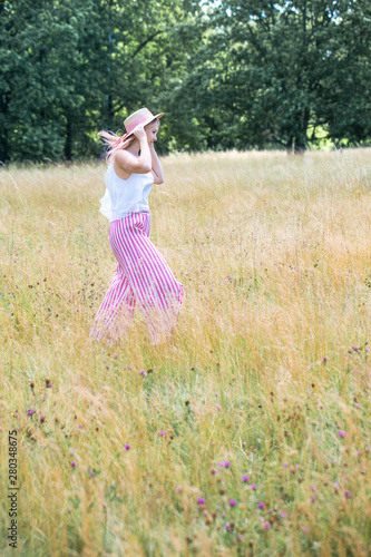 Young beautiful girl with pink hair in the summer hat walking in the golden field