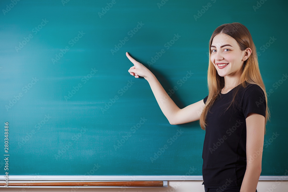 Beautiful sudent girl shows on empty copy space on the school board. Education concept. Beautiful sudent girl shows on empty copy space on the school board. Education concept.