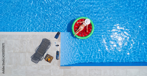 Aerial view of young woman in a white bikini is chilling on a red rubber mattress in the transparent, blue water © Cara-Foto