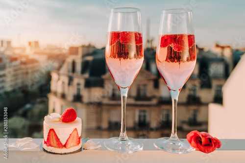 Paris luxury lifestyle. Pink champagne in two glasses, traditional french cake with strawberries on a balcony on the sunset