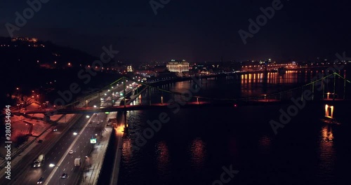 Night River  View On Colorful Rainbow Pedestrian Bridge With traffic on highway, Kyiv, Ukraine - Cityscape Aerial Flight, drone hyperlapse. photo