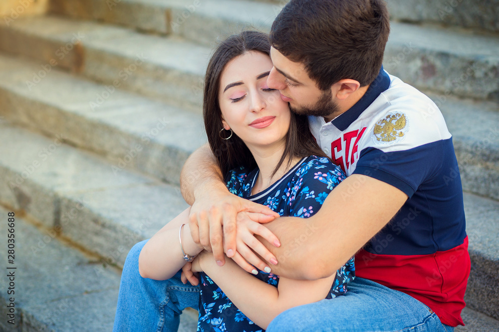The young loving couple of the Caucasian nationality sits on steps and embraces on city streets The young loving couple of the Caucasian nationality sits on steps and embraces on city streets