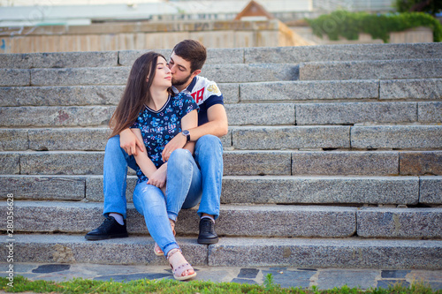 The young loving couple sits on steps and embraces on city streets