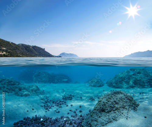 Underwater view of sandy and rocky bottom of the sea and blue sky. © magdal3na