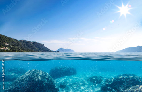 Underwater view of sandy and rocky bottom of the sea and blue sky. © magdal3na