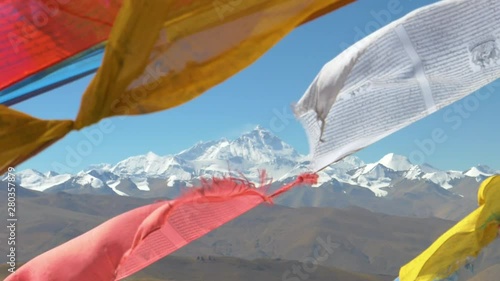 SLOW MOTION, CLOSE UP, DOF: Picturesque view of the snow covered Everest behind colorful prayer flags flapping in the wind. Mount Everest towering above the smaller barren hills in stunning Tibet.