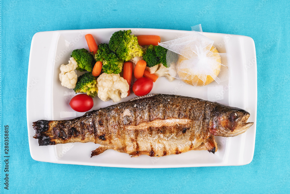 Mediterranean dish, European cuisine. whole fish baked in the oven, served with steamed vegetables - cauliflower, broccoli, carrots, cherry tomatoes and lemon Mediterranean dish, European cuisine. whole fish baked in the oven, served with steamed vegetables - cauliflower, broccoli, carrots, cherry tomatoes and lemon