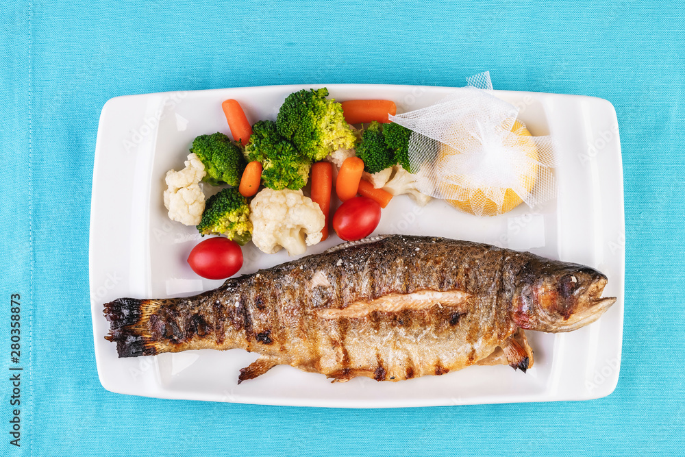 Mediterranean dish, European cuisine. whole fish baked in the oven, served with steamed vegetables - cauliflower, broccoli, carrots, cherry tomatoes and lemon Mediterranean dish, European cuisine. whole fish baked in the oven, served with steamed vegetables - cauliflower, broccoli, carrots, cherry tomatoes and lemon