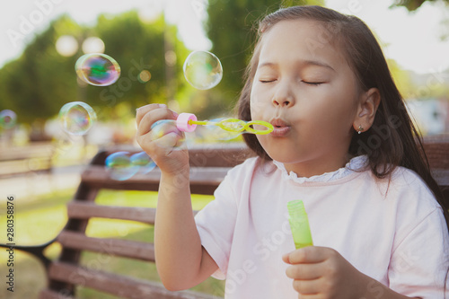 Close up of a cute little Asian girl having fun outdoors in the park, blowing bubbles. Adorable child blowing bubbles on a summer day in the park, copy space
