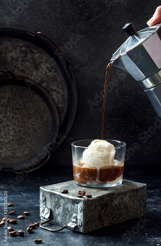 Female hand pouring coffee on vanilla ice cream to make an affogato coffee. Summer coffee drink with ice cream and espresso in the glass photo