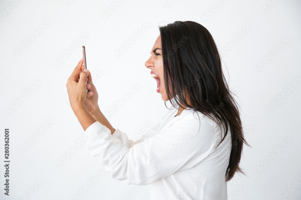 Crazy mad beautiful woman talking on speaker. Angry furious young Latin woman in white shirt shouting loud at smartphone. Negative emotions concept Crazy mad beautiful woman talking on speaker. Angry furious young Latin woman in white shirt shouting loud at smartphone. Negative emotions concept