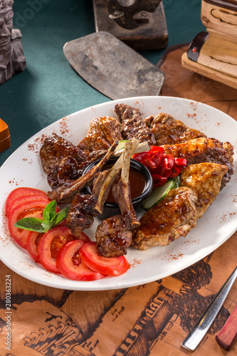 Assorted delicious grilled bbq meat with tomatoes on white plate on old map background