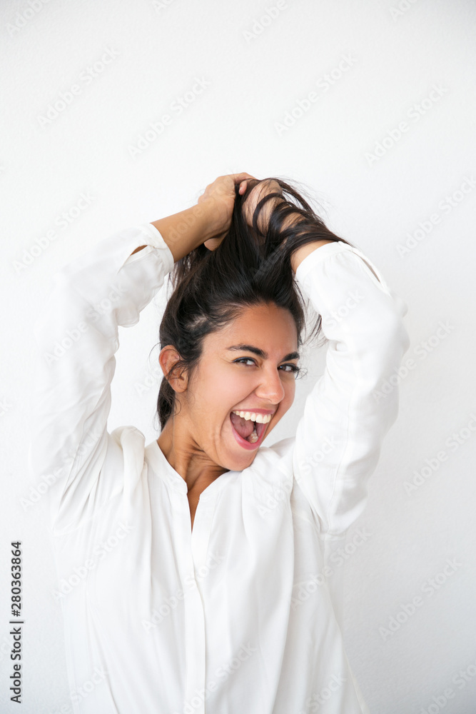 Overjoyed excited woman rejoicing at good news and having fun. Happy young Latin woman in white shirt holding hair overhead, smiling and shouting for joy. Joy concept Overjoyed excited woman rejoicing at good news and having fun. Happy young Latin woman in white shirt holding hair overhead, smiling and shouting for joy. Joy concept