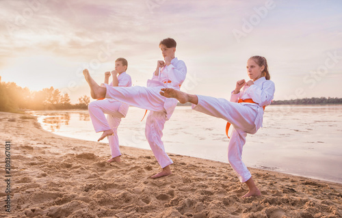 group of kids training karate martial arts on sunset beach photo