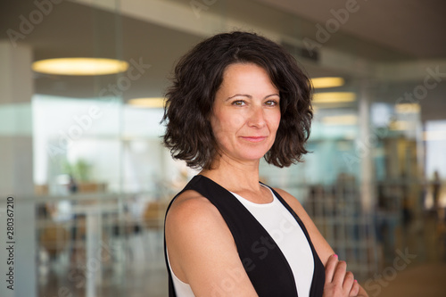 Free Download Positive confident business woman in casual posing in office hall. Middle aged businesswoman with folded arms standing near glass wall, looking at camera and smiling. Confident woman concept - GFXLoad