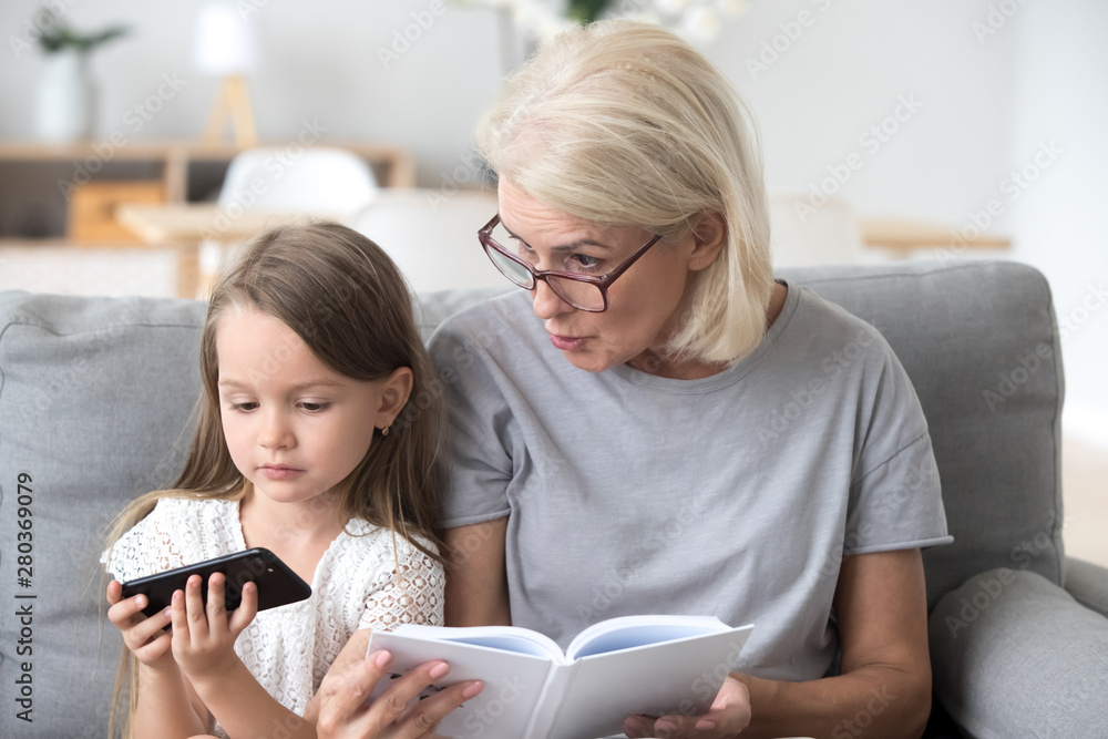 Serious grandma and little granddaughter sitting on couch Serious grandma and little granddaughter sitting on couch