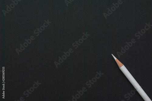 White (chalk) pencil lies diagonally on black paper. School, business template or blank.