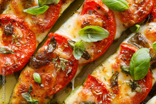 Roasted, stuffed zucchini with the addition of tomatoes, mozzarella cheese, fresh basil and olive oil (caprese salad) in a ceramic baking dish, close-up, top view. Nutritious and tasty vegetarian dish