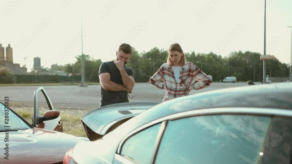 View of upset stressed drivers looking on broken stuck cars on the roadside. Two people man and woman talk argue on bad situation wait for the police outdoors.