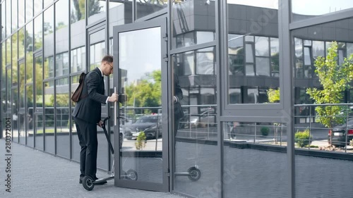 Wallpaper Mural businessman in formal wear riding kick scooter, opening door and entering building Torontodigital.ca