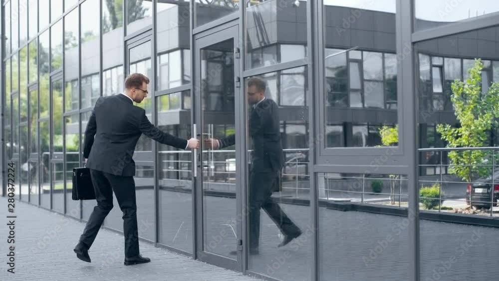 businessman in formal wear with briefcase opening door and entering building businessman in formal wear with briefcase opening door and entering building